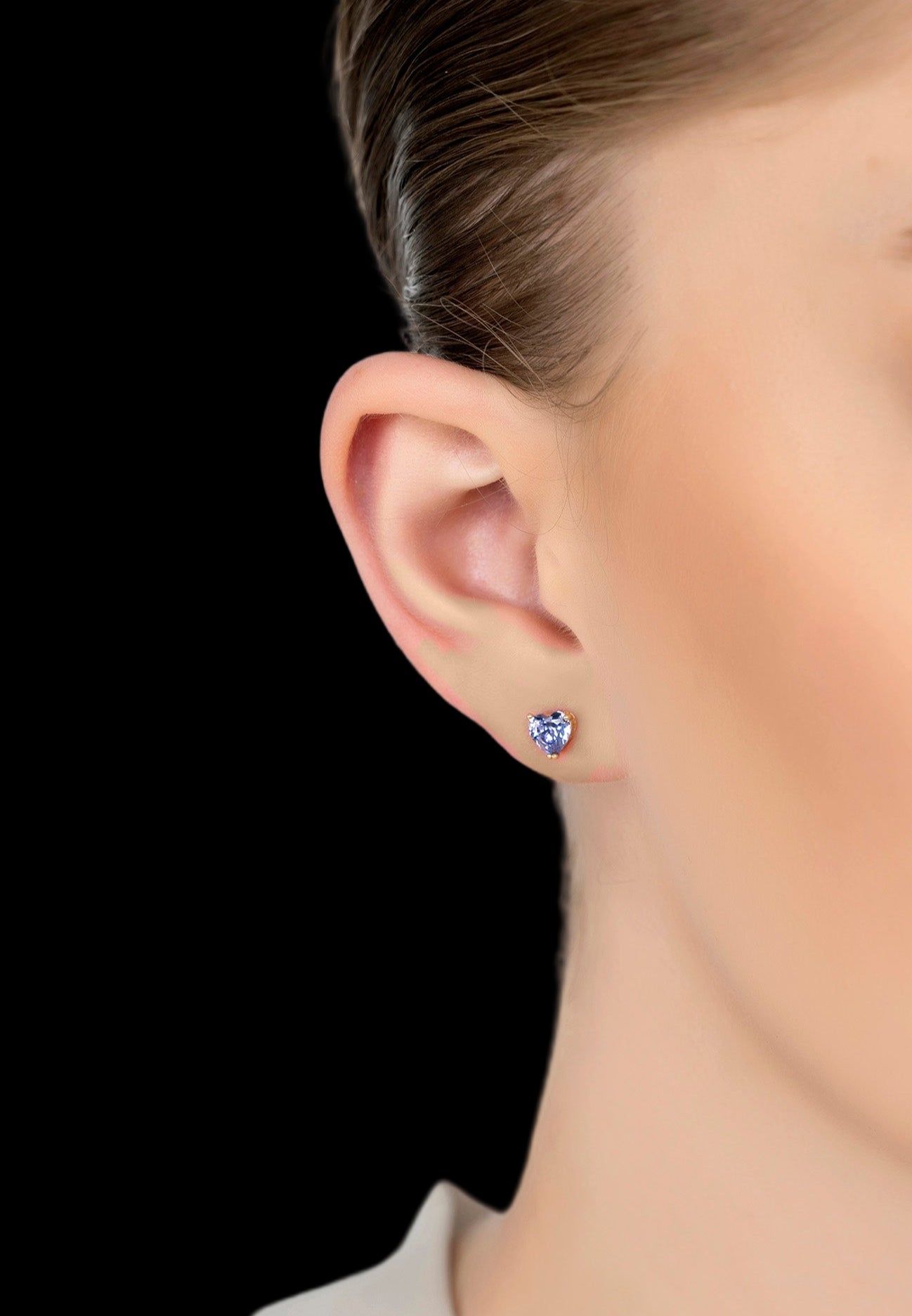 Close-up of a person wearing a blue gemstone stud earring on a white background