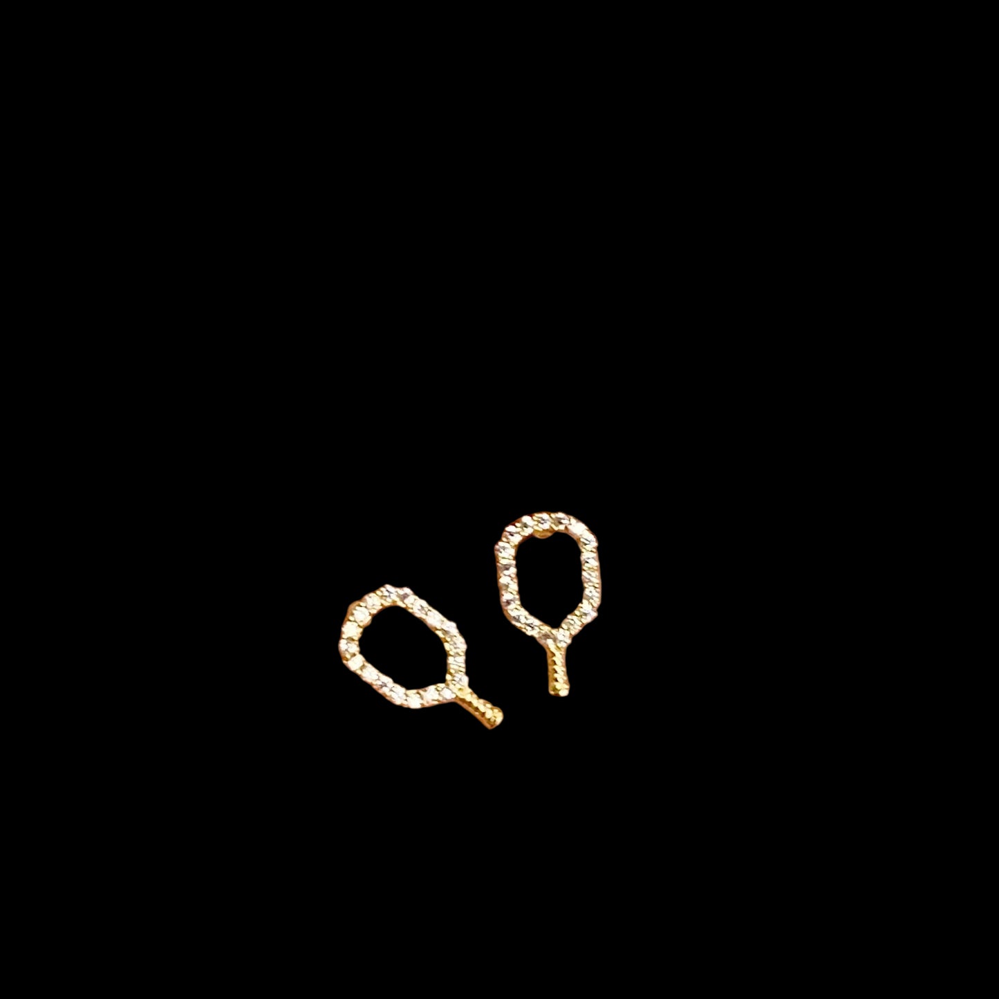 Gold tennis racket earrings on a hand with a natural background
