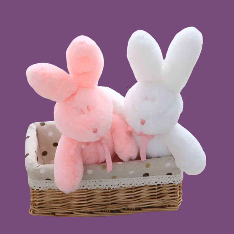 Two plush bunny toys, one pink and one white, in a wicker basket with a polka dot pattern.