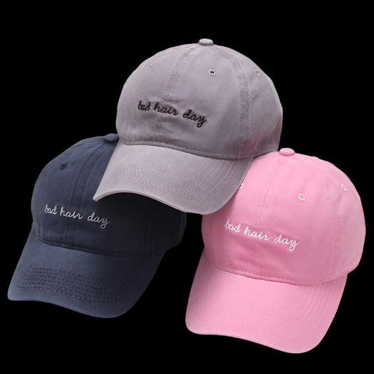Three baseball caps in gray, navy, and pink with 'bad hair day' text on a white background