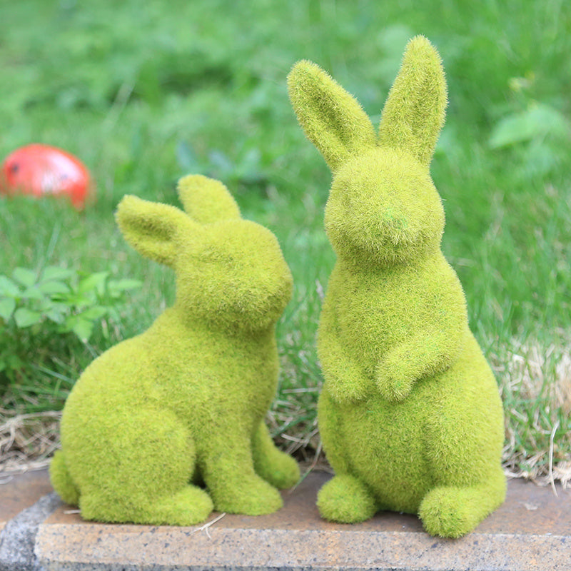 Two moss-covered rabbit sculptures on a stone surface with a grassy background.