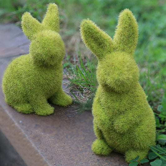 Two moss-covered rabbit sculptures on a stone surface with grass in the background