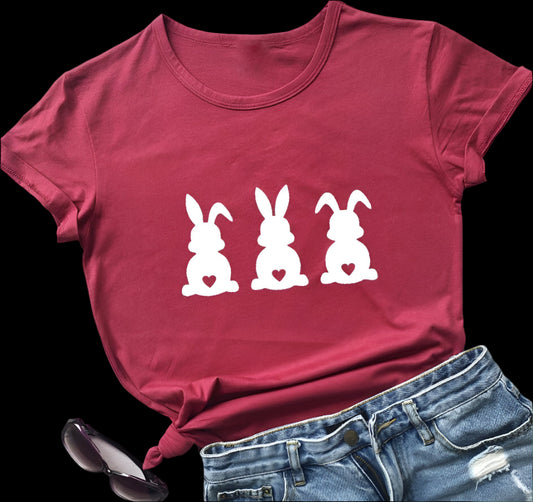 Red t-shirt with white bunny graphics on a wooden surface with jeans and sunglasses.