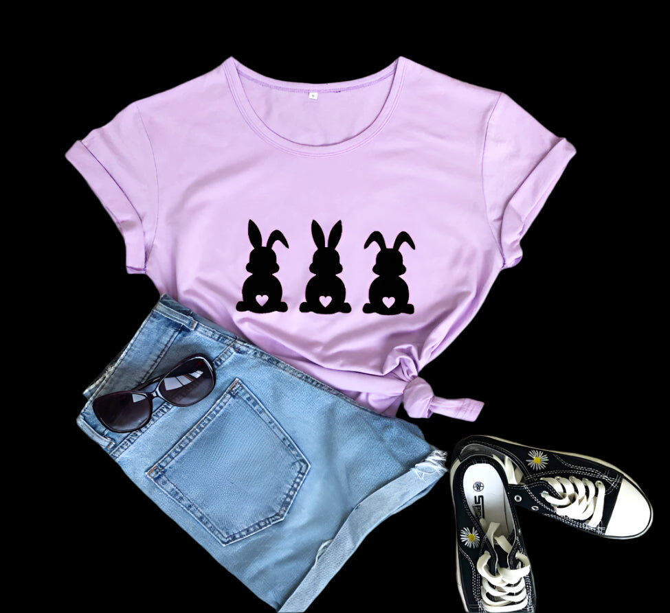 Pink t-shirt with black rabbit prints, denim shorts, sunglasses, and sneakers on a wooden surface