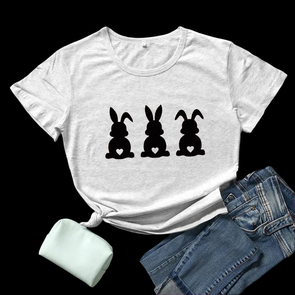 White t-shirt with black bunny graphic on a wooden surface with sunglasses and jeans.