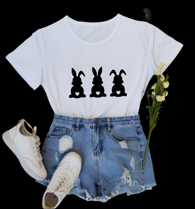White t-shirt with black rabbit illustrations, blue denim shorts, white sneakers, and flowers on a wooden surface.