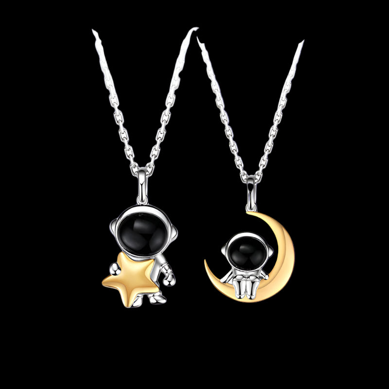 Two pendants shaped like an astronaut on a star and a moon with black gemstones on a dark blue background.
