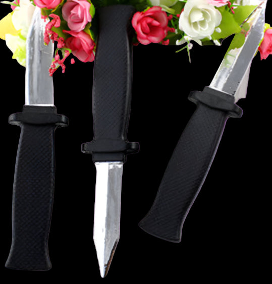 Three small knives with black handles on a white surface with flowers in the background