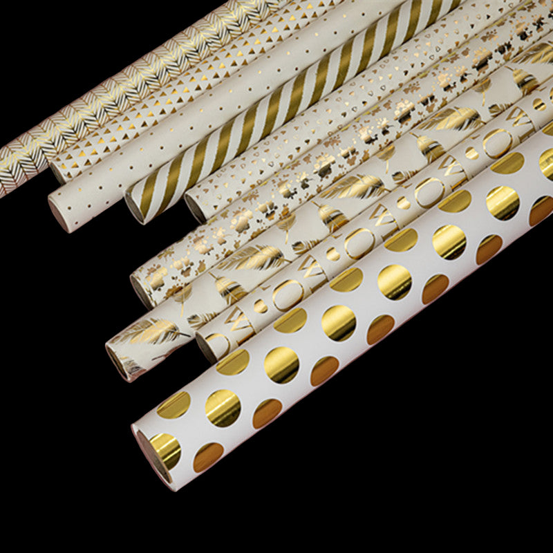 Rolls of gold and white patterned wrapping paper on a pink background