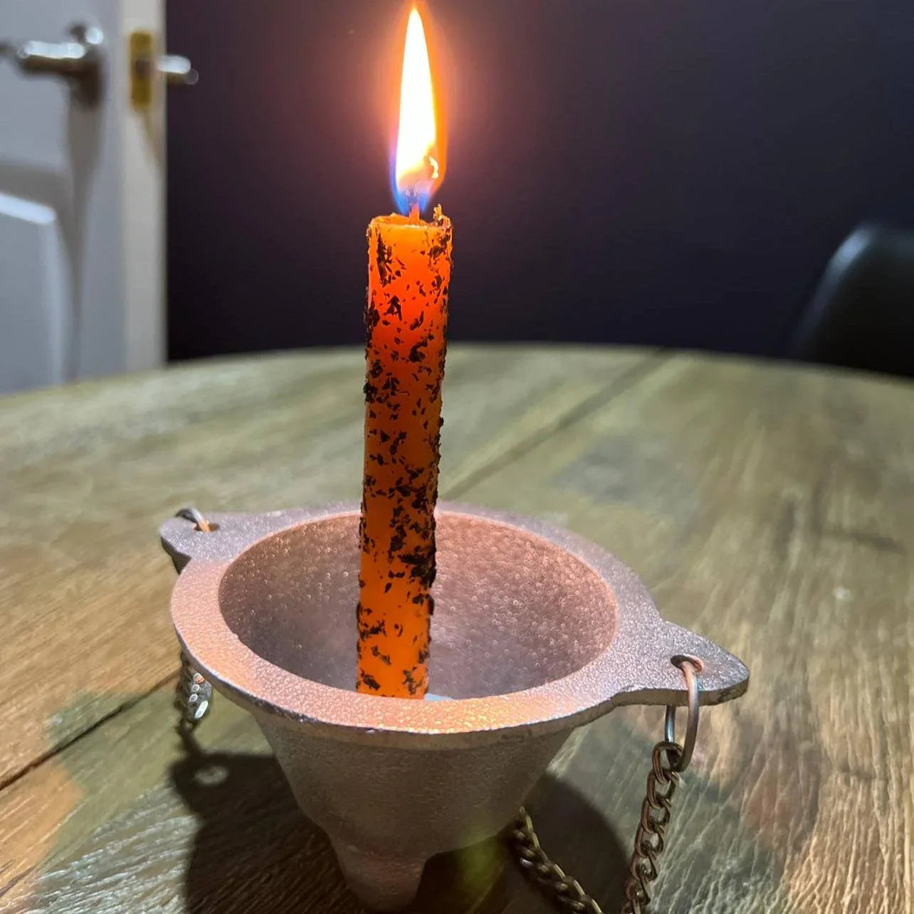 Orange candle with a chain in a metal holder on a wooden surface