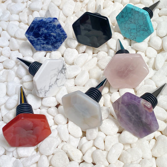 Set of colorful gemstone bottle stoppers on a white pebble background