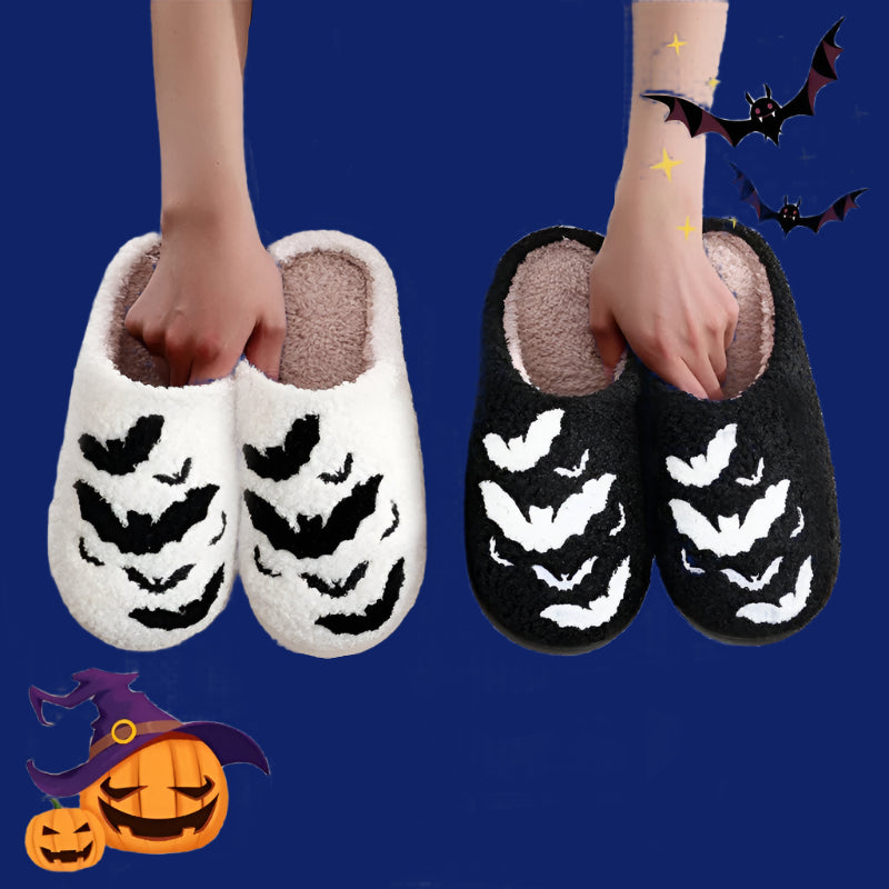 Pair of Halloween-themed slippers with bat designs held by a person on a white background.