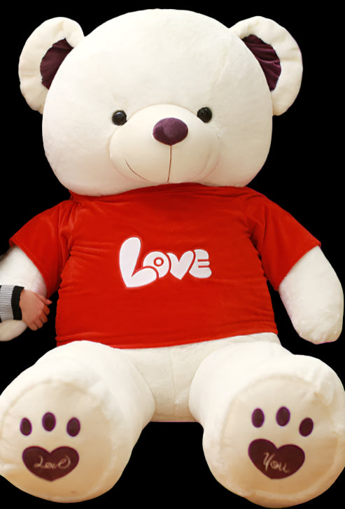 Woman sitting next to a large white teddy bear wearing a red shirt with 'LOVE' on it in a library setting.
