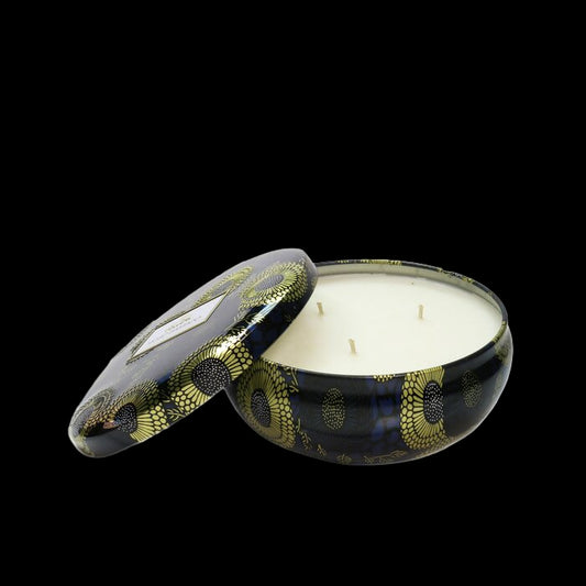 Candle in a decorative black tin with gold patterns on a white background