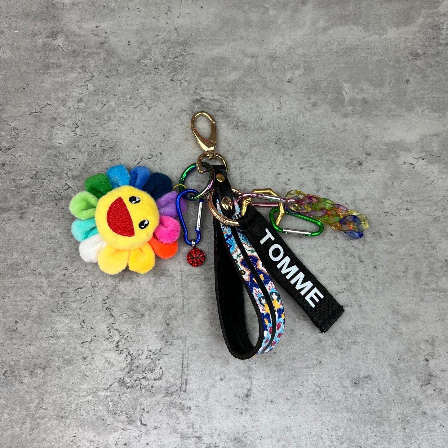 Keychain with colorful flower charm and 'TOMME' strap on a concrete surface