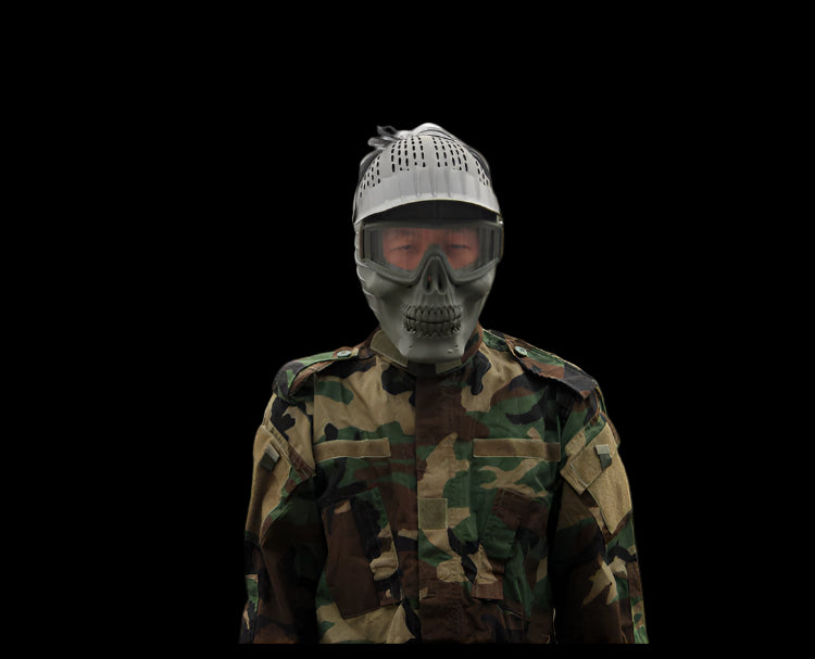 Person wearing a camouflage jacket and skull-themed mask with buildings and trees in the background