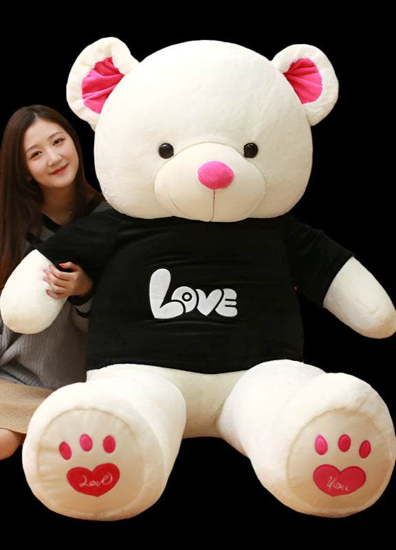 Person sitting next to a large white teddy bear wearing a black shirt with 'LOVE' on it, in a room with bookshelves.