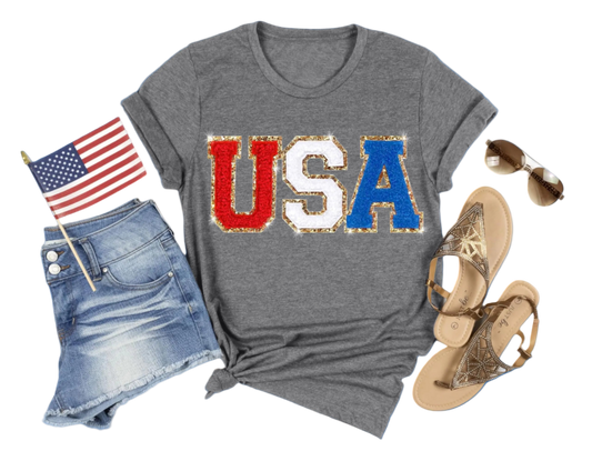 Gray t-shirt with 'USA' print, denim shorts, sandals, and American flag on a white background