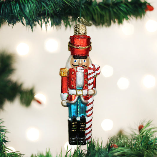 Decorative nutcracker ornament hanging on a Christmas tree with lights in the background.