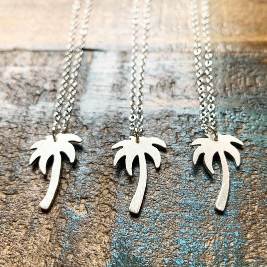Three silver palm tree necklaces on a wooden surface
