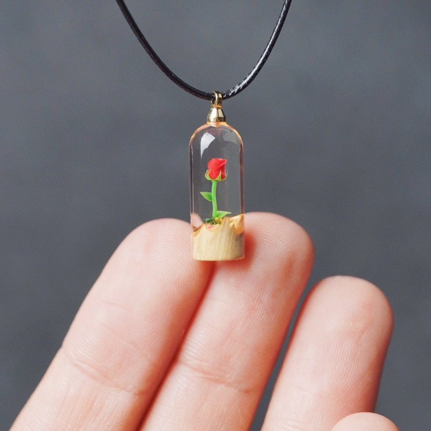 Glass pendant with a red rose inside held between fingers against a dark background