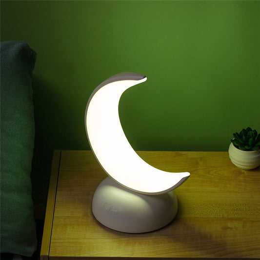 Moon-shaped night light on a wooden surface with a green wall background