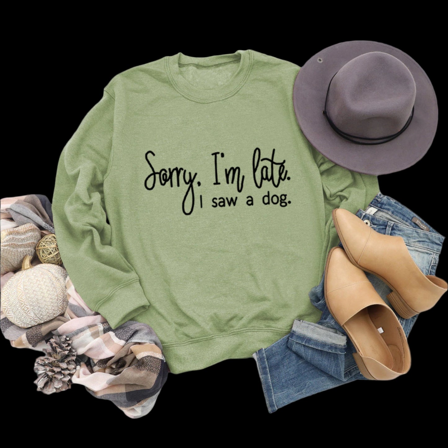 Green sweatshirt with text, hat, boots, and jeans on a wooden surface