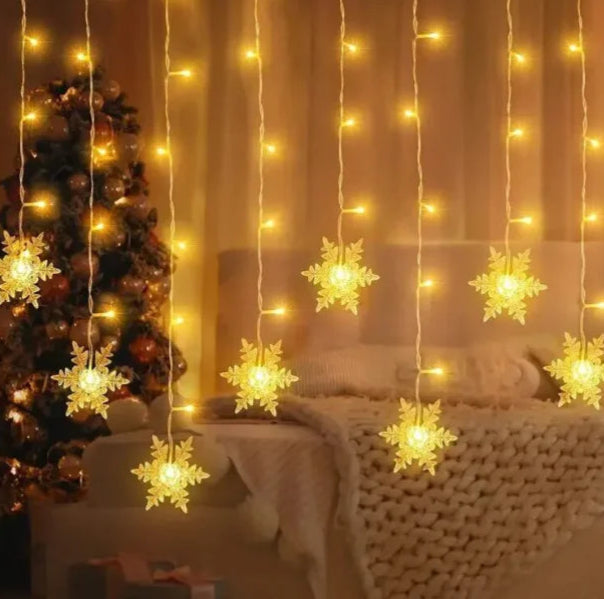 Decorative string lights with snowflake designs hanging in a room with a Christmas tree and sofa.