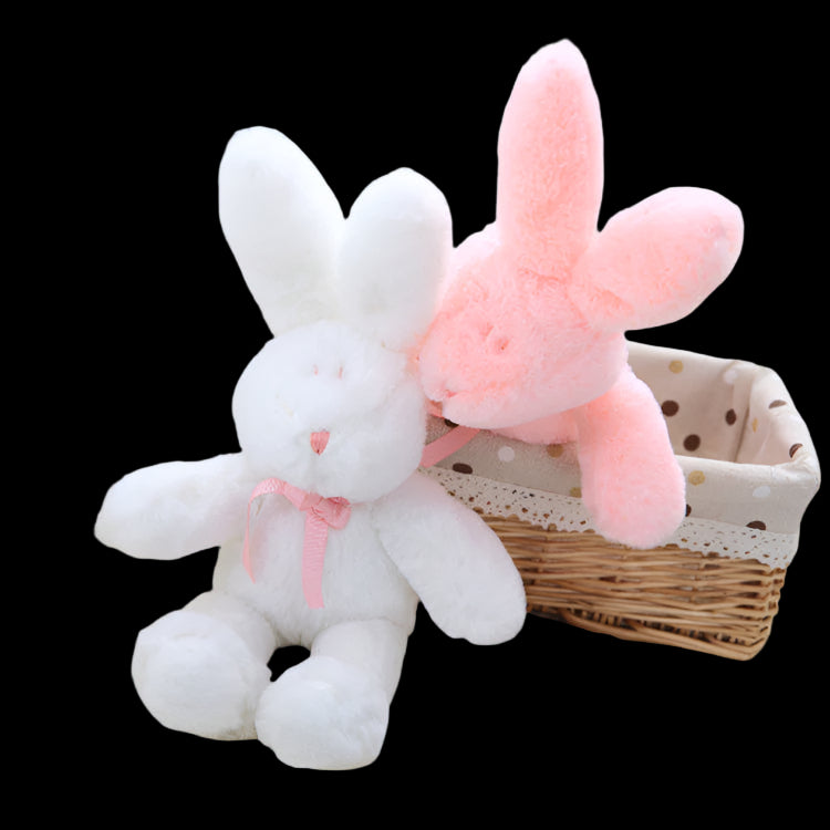Two plush toys, a white rabbit and a pink bunny, sitting on a soft surface with a basket in the background.