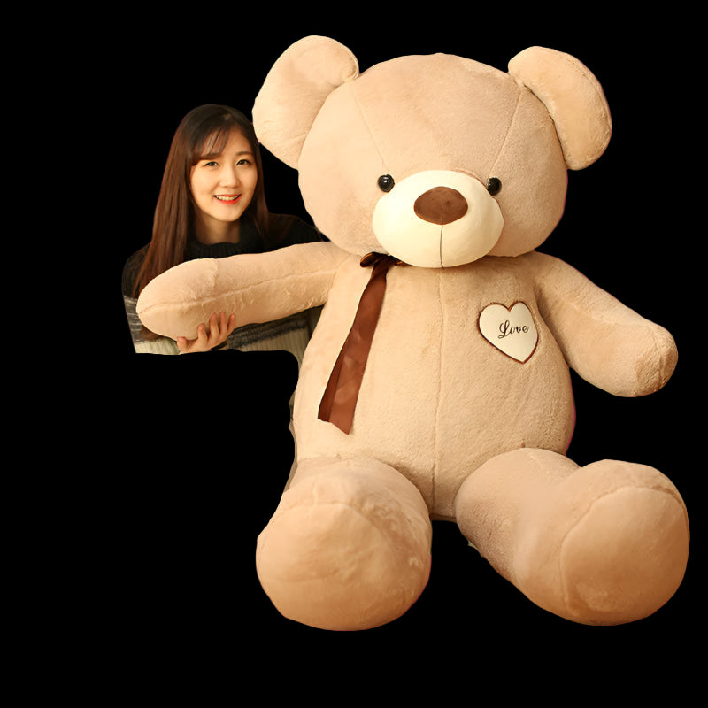 Woman sitting next to a large teddy bear with a heart and 'Love' text on a wooden floor.