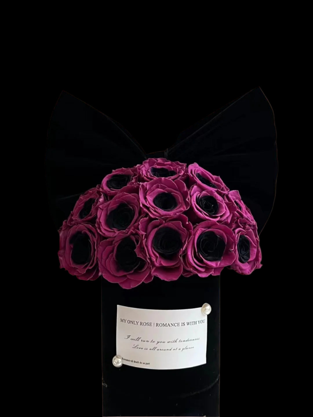 Bouquet of purple roses in a black container with a bow on a reflective surface.