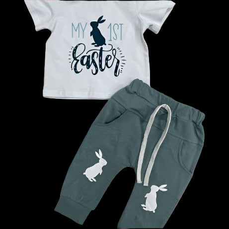 Children's outfit with 'My 1st Easter' shirt and green pants with bunny designs on a concrete floor.