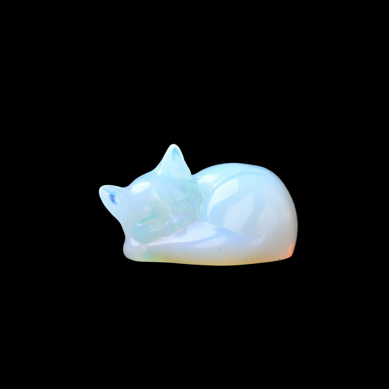 Opalite cat figurine on a dark surface with blurred greenery in the background
