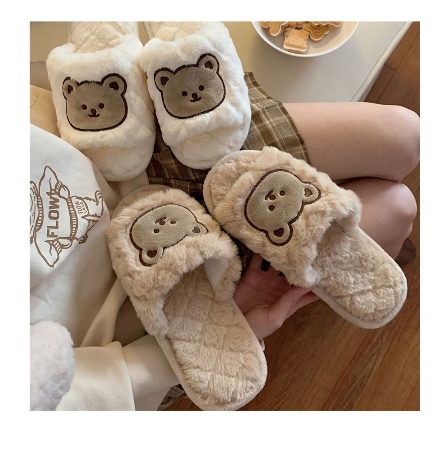 Pair of white slippers with bear face design worn by a person on a wooden floor.