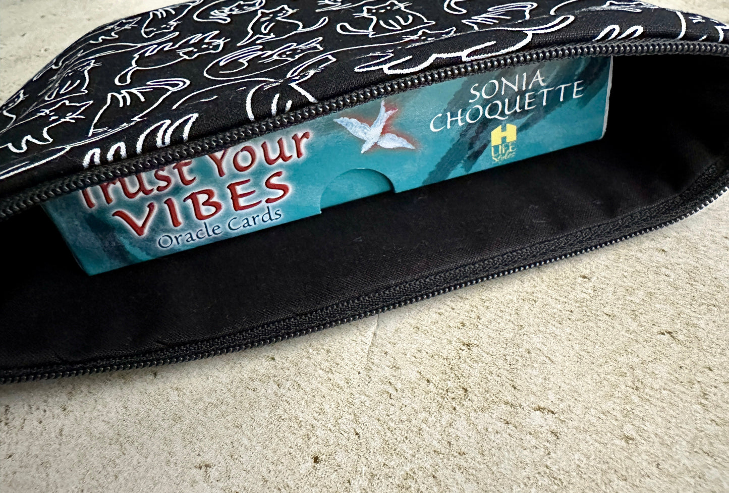 Black pouch with 'Trust Your Vibes' text and oracle cards inside on a beige surface