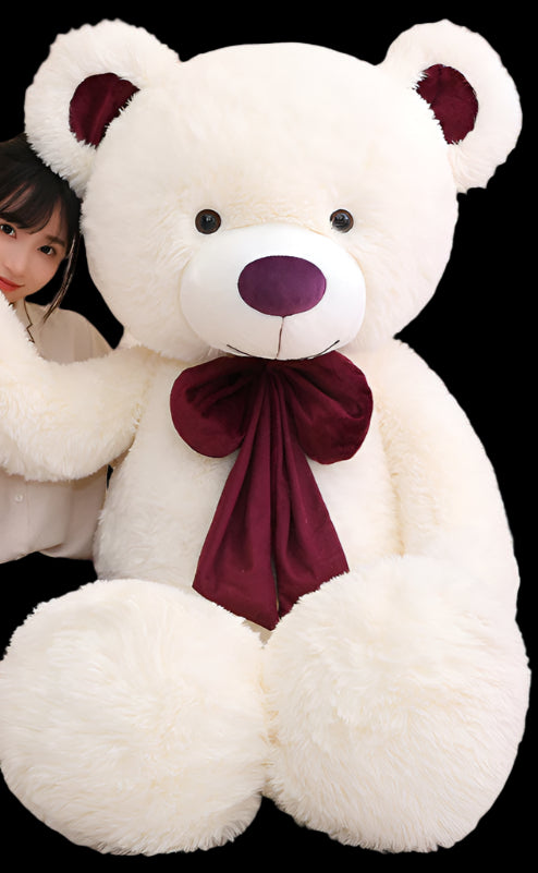 Person holding a large white teddy bear with a red bow in a room.
