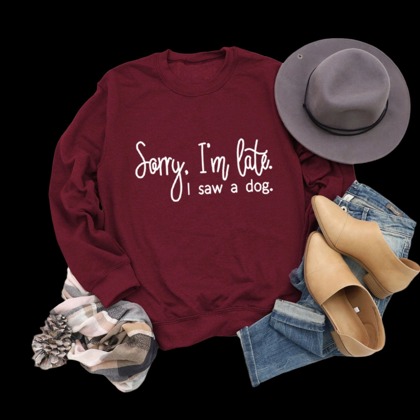 Maroon sweatshirt with text, gray hat, jeans, boots, and plaid scarf on a wooden surface