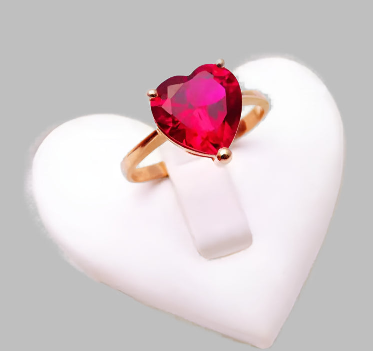 Ring with a heart-shaped red gemstone on a white heart-shaped stand