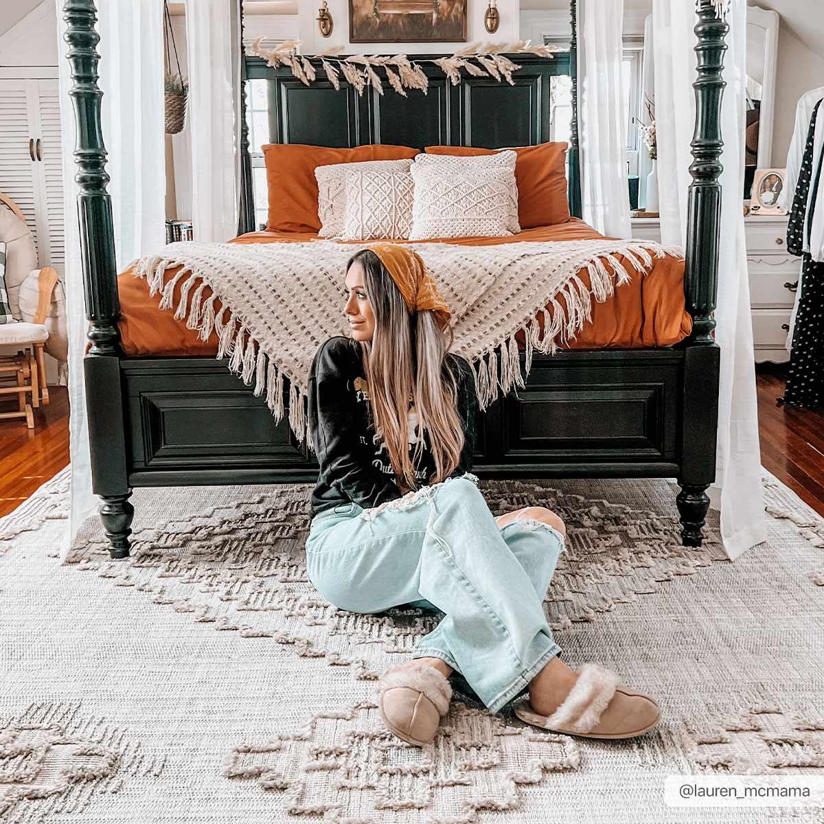 Woman sitting on the floor in a bedroom with a four-poster bed and decorative pillows.