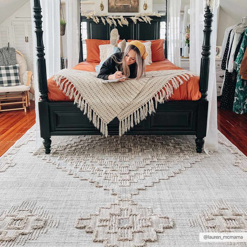 Woman lying on a bed with orange pillows and a white blanket, surrounded by home decor.