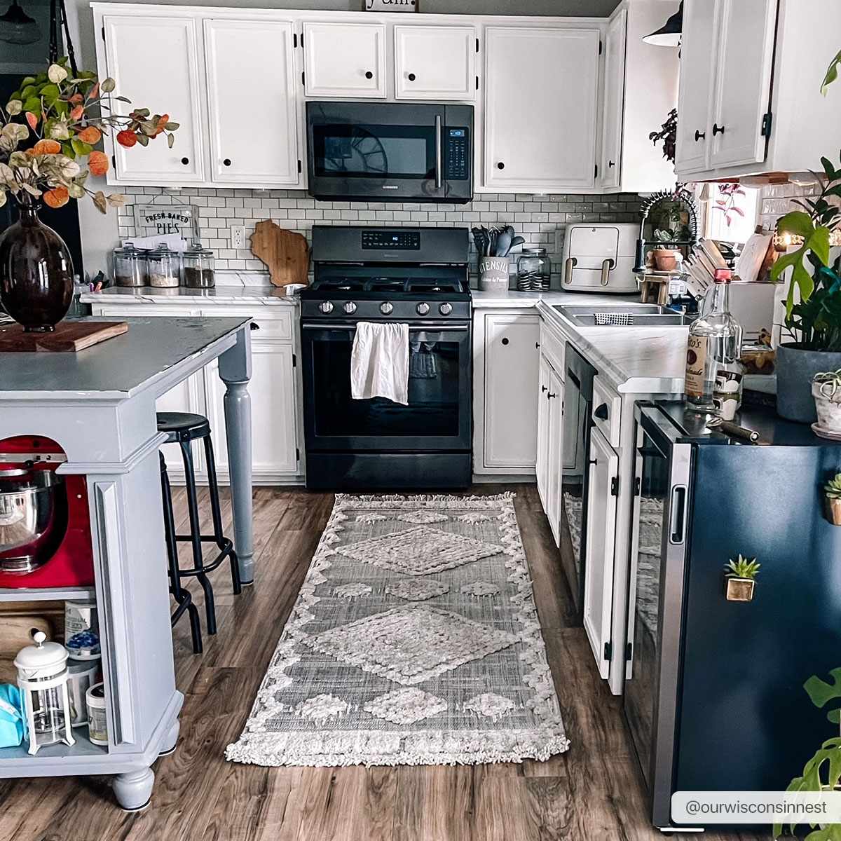 Modern kitchen with white cabinets, black appliances, and a blue island.