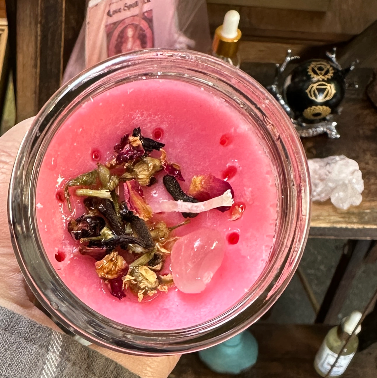 Hand holding a pink candle with dried herbs in a store setting