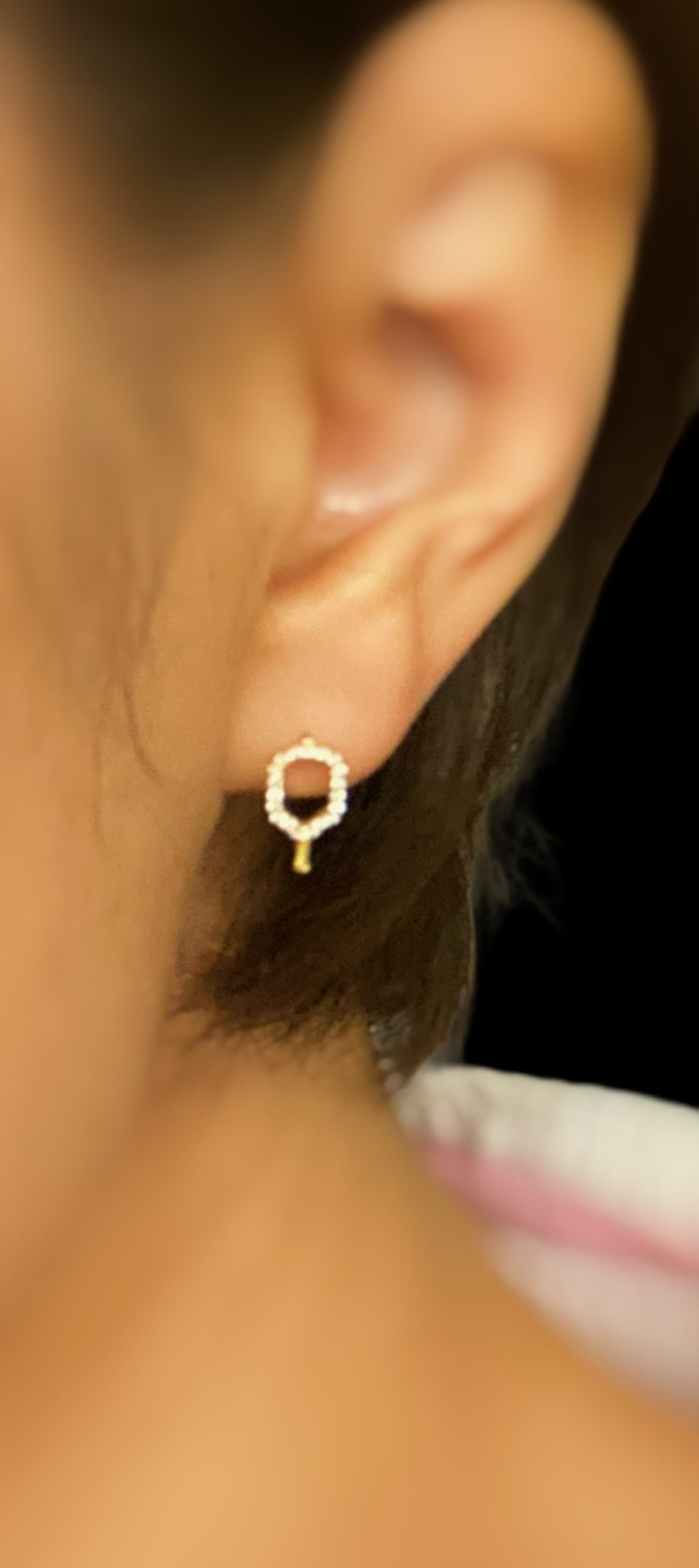 Close-up of an ear wearing a gold hoop earring with a blurred natural background