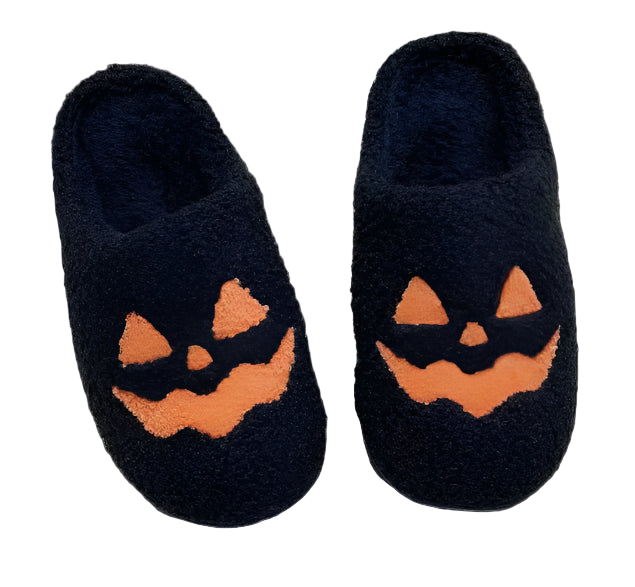 Black slippers with jack-o'-lantern faces on a white blanket