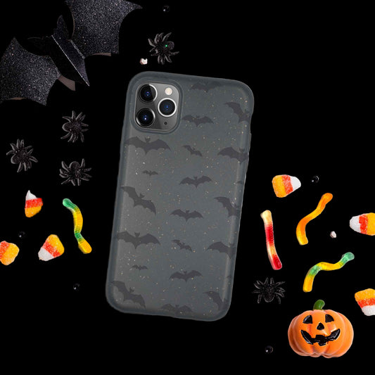 Phone case with bat pattern surrounded by Halloween-themed decorations on a light gray background