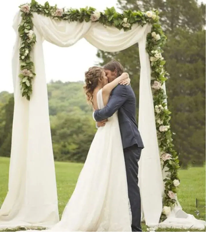 Couple embracing under a floral archway in a park setting