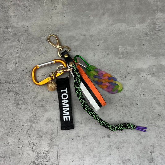 Colorful keychain with 'TOMME' tag on a gray concrete surface