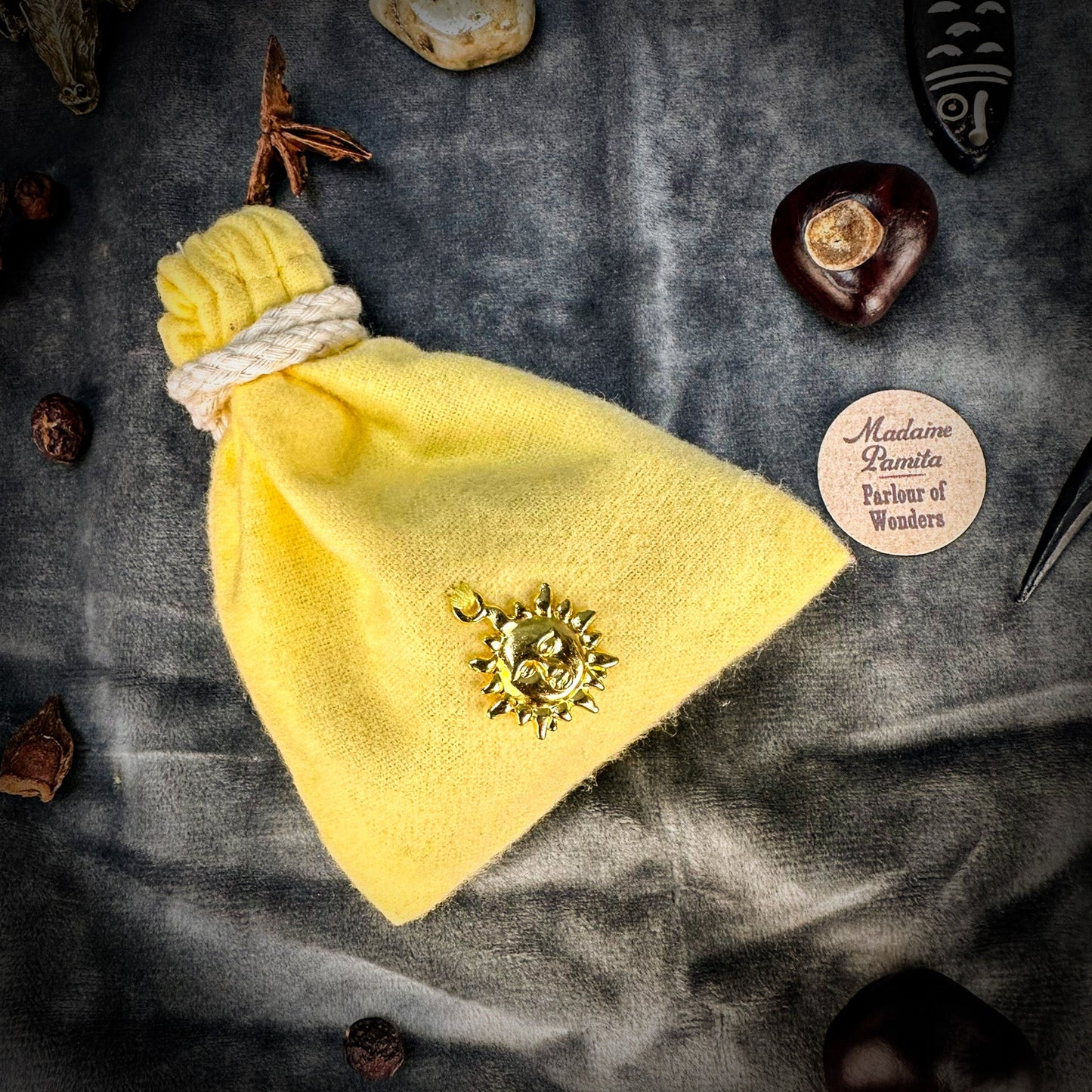 Yellow drawstring bag with a sun emblem on a textured surface with decorative items.