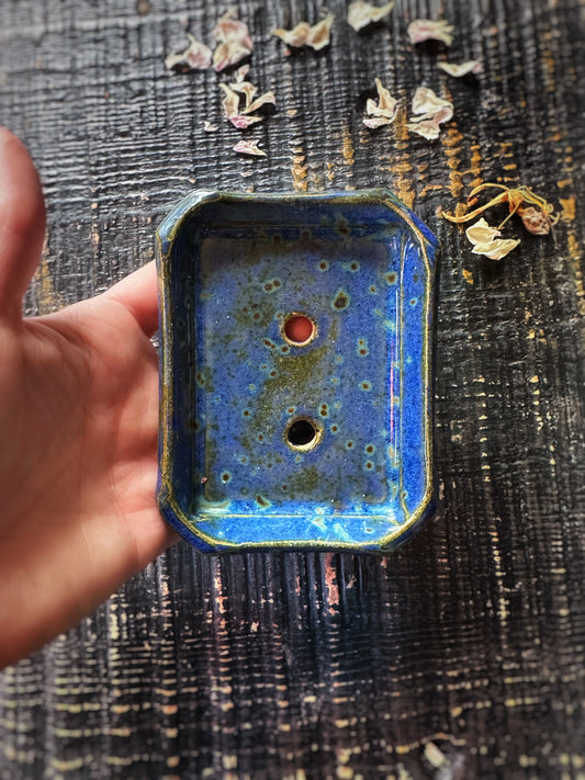 Hand holding a blue ceramic object with a textured surface against a dark textured background.