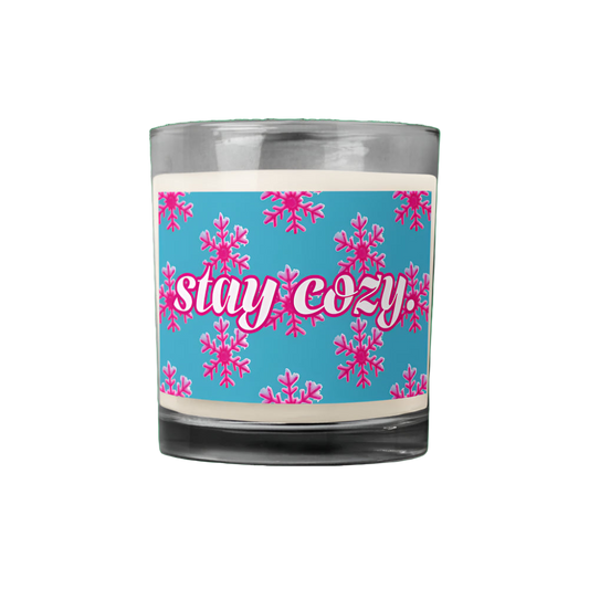 Candle with a blue label featuring pink snowflakes and 'stay cozy' text on a white background.